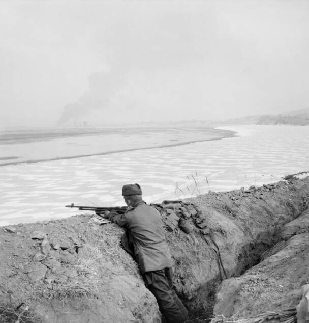 WAR ZONE: An American sentry armed with an automatic rifle surveys a fire in Seoul from a slit trench overlooking the frozen Han River in 1951. Photo: Australian War Memorial