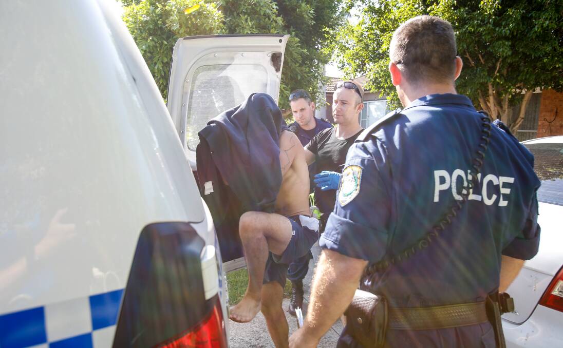 UNDER ARREST: A man conceals his face as he steps into a police paddy wagon at the Collaery Road address. Picture: Adam McLean