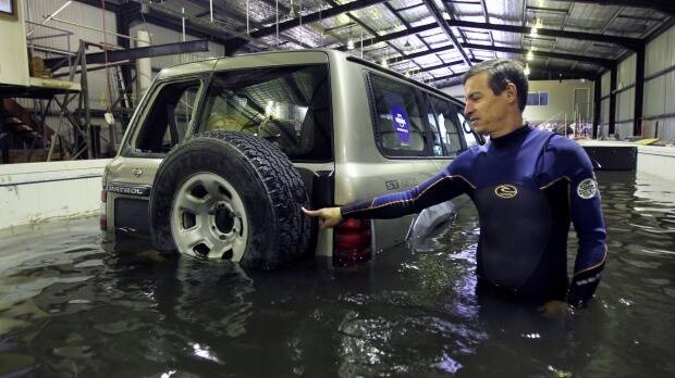 UNSW researcher Grantley Smith moves a four-wheel drive with his fingertip after it begins to float in a floodwater simulation. Photo: Tony Walters