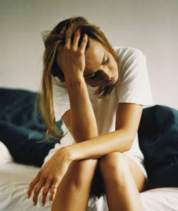 Young woman sitting on edge of bed, holding head in hand Photo: Mark Douet