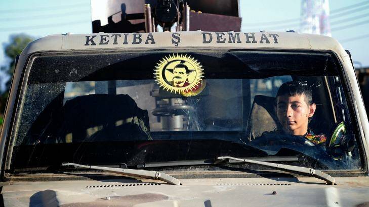A young YPG fighter sits in a car in the village of Tel Marouf, the face of PKK founder Abdullah Ocalan on the windscreen. 
  Photo: Fadi Yeni Turk