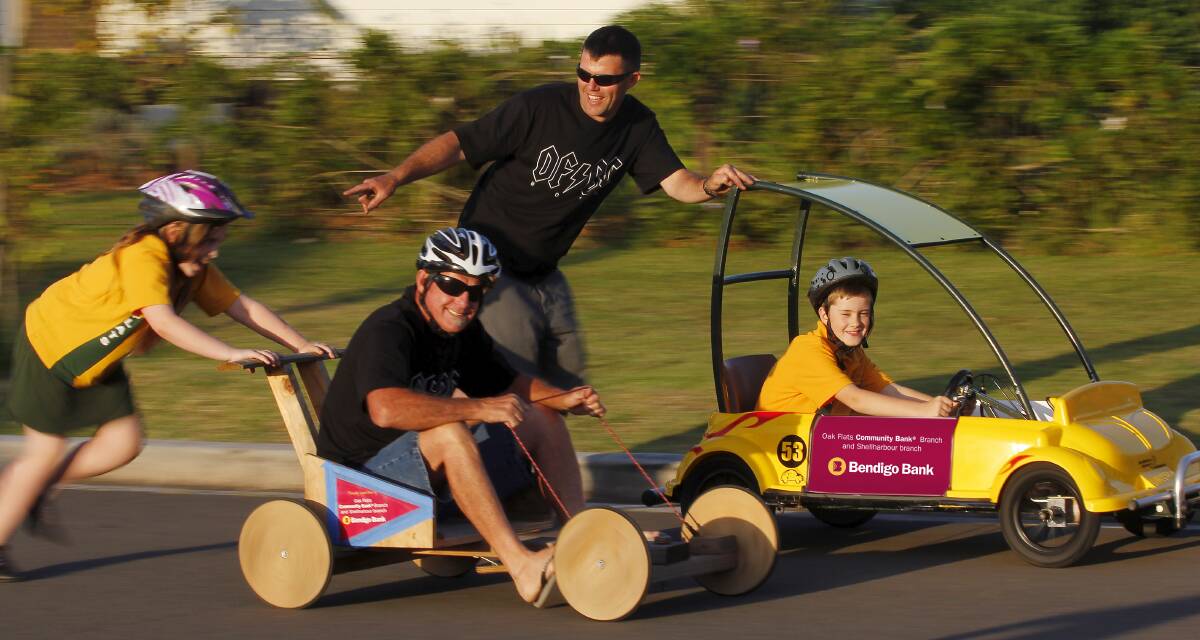 Granddad Mark Tolley (left) and dad Michael Austin give Oak Flats Public School students Hannah Austin and Thomas Cormack a test ride in a couple of the carts.