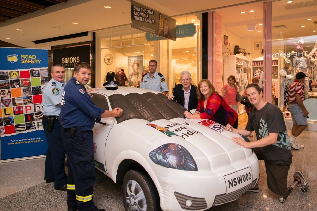 NSW Traffic and Highway Patrol officer Kevin Hood, State Fire Service officer Frank Lampe, Shellharbour SES officer Martin Sewell, Shellharbour City Council general manager Michael Willis, Shellharbour Mayor Marianne Saliba and supporter of Fatality Free Friday Brett Stibners put their signatures on the inflatable car at Stockland Shellharbour. Picture: ALBEY BOND