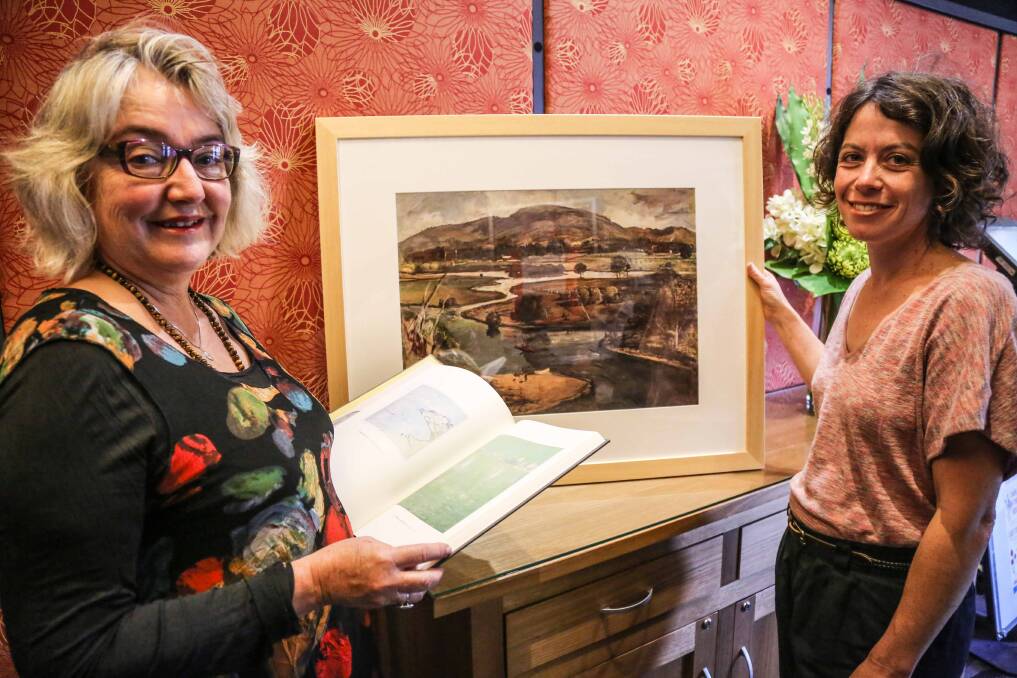 Gerringong Bowling Club director Sandra McCarthy and Penny Sadubin with the new book of Lloyd Rees' works and one of his paintings ahead of the launch of his exhibition at the club. Picture: GEORGIA MATTS