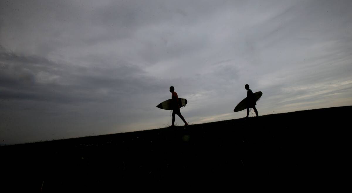 Surfers are silhouetted against a grey sky. Picture: Sylvia Liber
