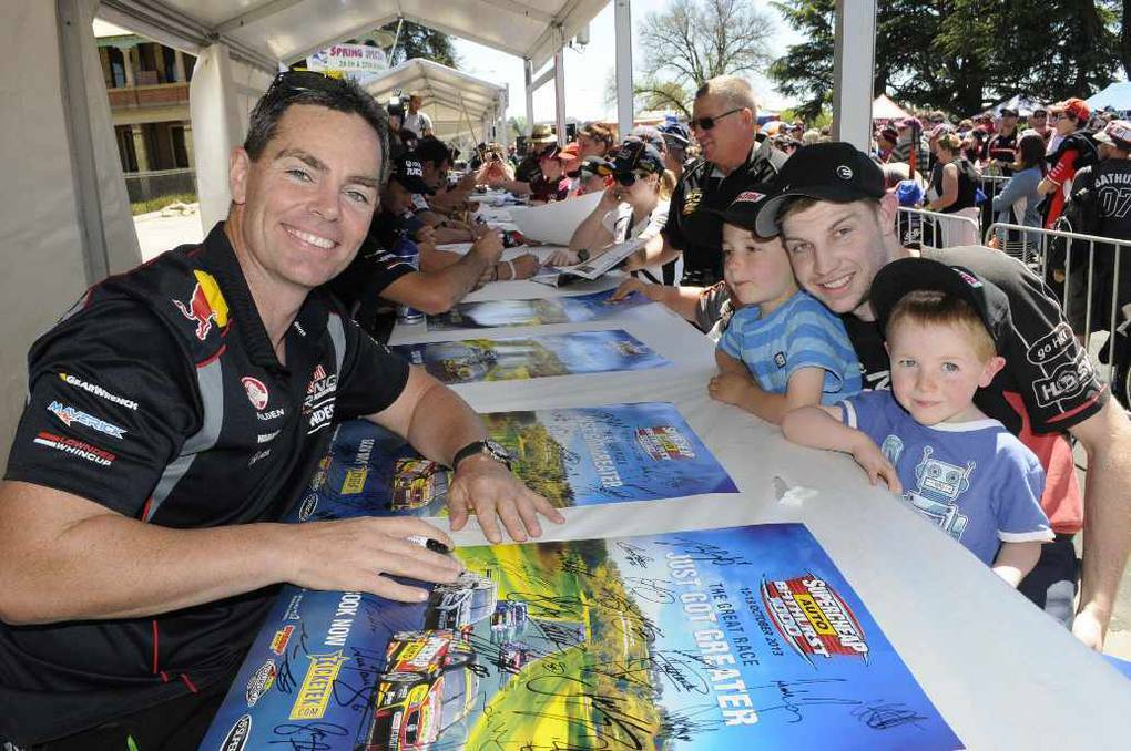 Craig Lowndes signs some posters for Nathaniel Mason with his nephews, Dominic (6) and Aiden Poisel(4) ahead of the Bathurst 100. PHOTO: Chris Seabrook.