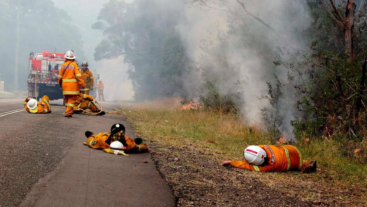 NEWCASTLE HERALD: Exhausted firefighters take a rest while fire burns beside them in Cragan Bay Road, Nords Wharf. Photo by PHIL HEARNE 