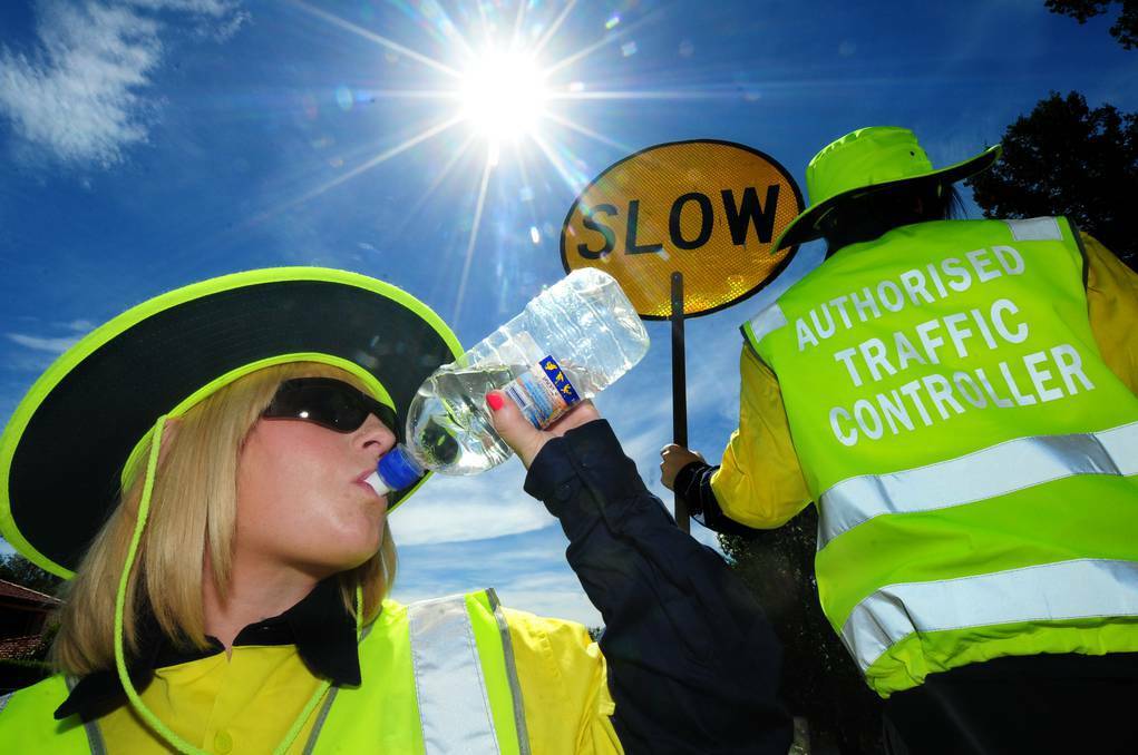 DUBBO: Working safely in yesterday's top of 34 degree heat is Elaine Collins drinking water and Christine Kennedy holding the sign. Photo: LOUISE DONGES