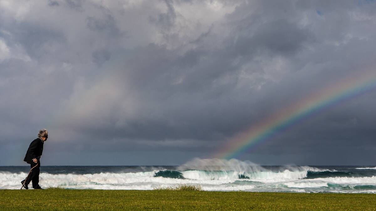 A women walks along Kiama Surf Beach where big seas and rainbows were on show. Picture: DYLAN ROBINSON