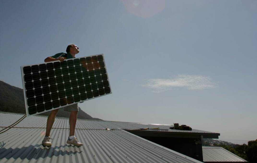 A man carries a solar panel across a roof. Picture by Kirk Gilmour